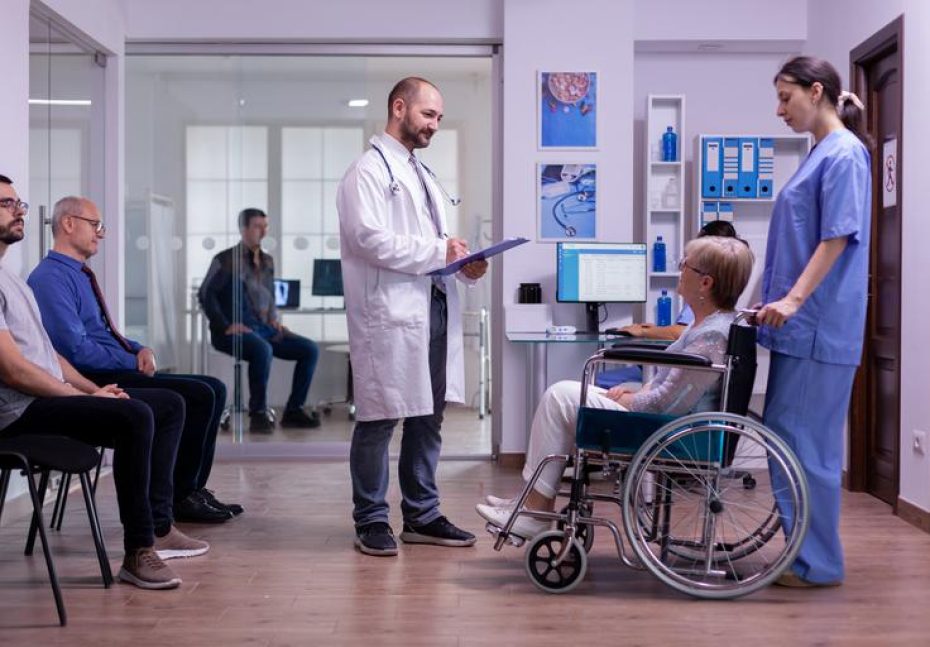Doctor checking diagnosis of paralyzed, disabled senior woman in wheelchair sitting in reception room of hospital. Medical staff taking care of invalid elderly patient, man waiting in examination room
